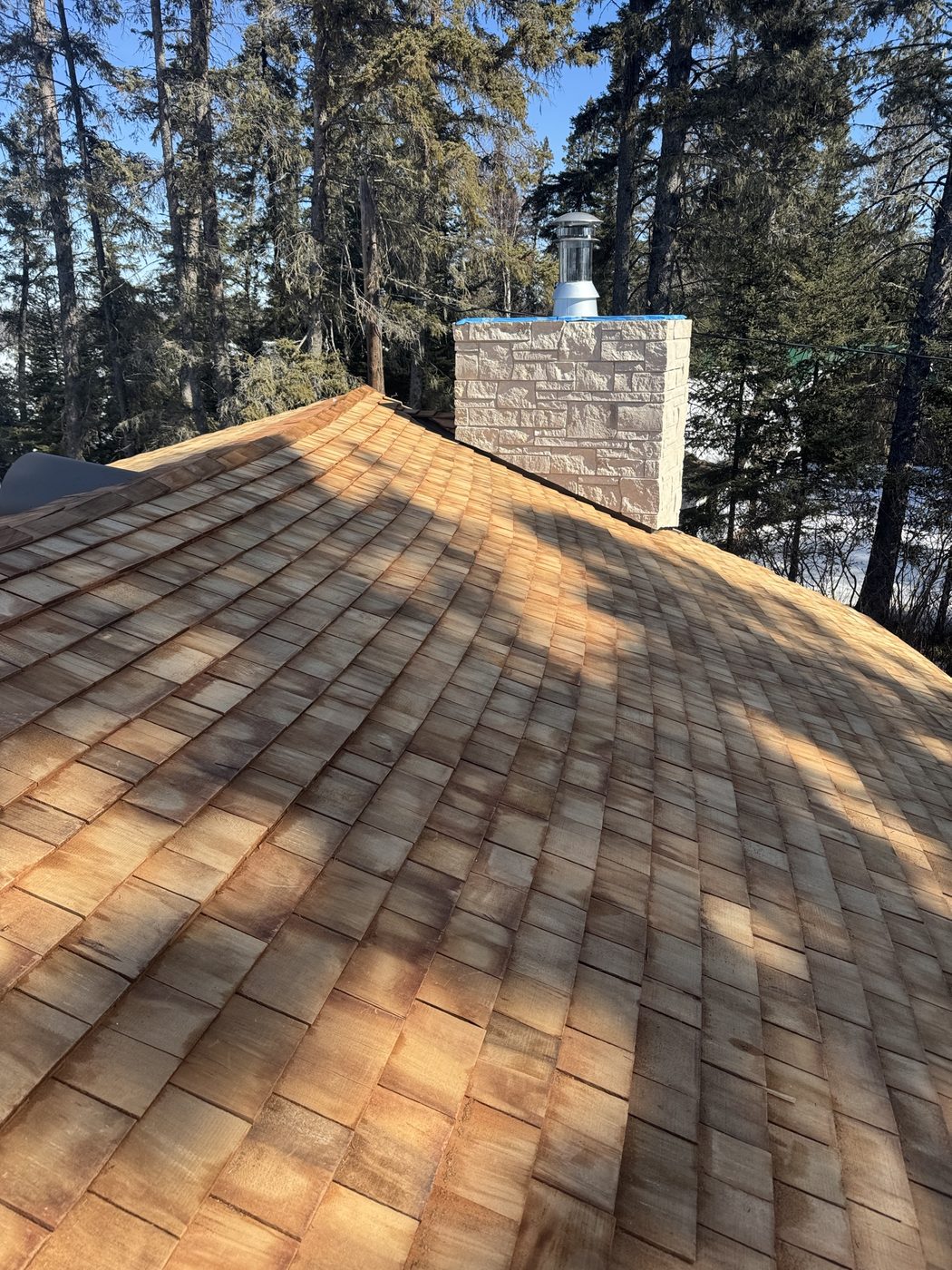 Cedar shake roof with a stone chimney on a Westman home